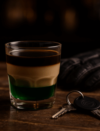 Harley Davidson cocktail recipe in a rocks glass with layered green, cream, and dark tones beside motorcycle keys