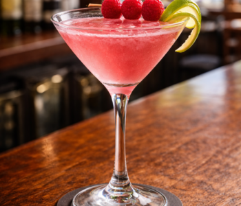 A heavenly hilary cocktail recipe served in a cocktail glass with raspberry garnish and lime twist on a neighborhood bar counter.