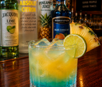 A liam's lucky charm cocktail recipe served in an old fashioned glass with pineapple and lime garnish on a neighborhood bar counter.