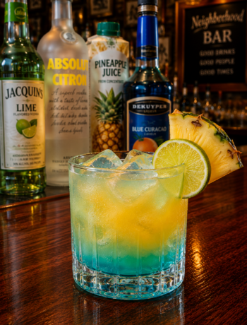 A liam's lucky charm cocktail recipe served in an old fashioned glass with pineapple and lime garnish on a neighborhood bar counter.