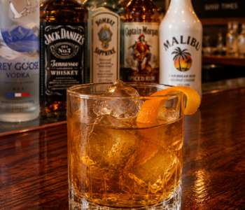 A master and commander cocktail recipe served in an old fashioned glass with large ice cubes and orange twist garnish on a neighborhood bar counter.