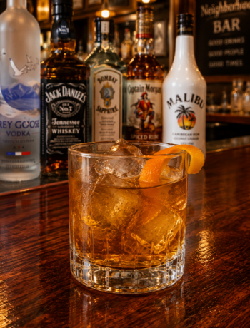 A master and commander cocktail recipe served in an old fashioned glass with large ice cubes and orange twist garnish on a neighborhood bar counter.