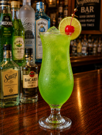 A midori madness cocktail recipe served in a hurricane glass with lime and cherry garnish on a neighborhood bar counter.