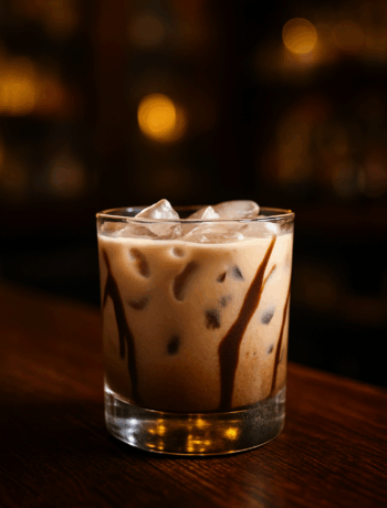 Mud Slide cocktail recipe in an old fashioned glass with ice and chocolate drizzle on a dark wooden bar