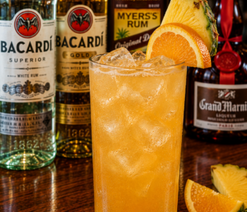 A navy grog cocktail recipe served in a Collins glass with pineapple and orange garnish on a neighborhood bar counter.