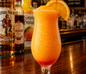 An orange push up cocktail recipe served frozen in a hurricane glass with orange slice and cherry garnish on a neighborhood bar counter.