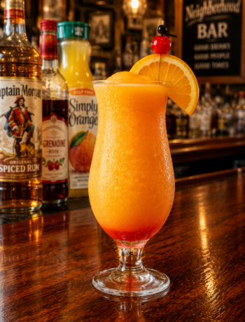 An orange push up cocktail recipe served frozen in a hurricane glass with orange slice and cherry garnish on a neighborhood bar counter.
