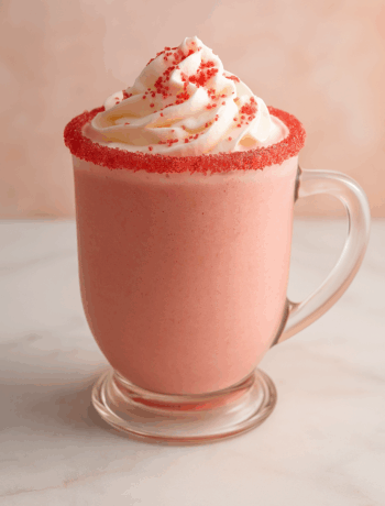 Raspberry Beret cocktail recipe served in a mug with whipped cream and red sugar rim on a marble surface