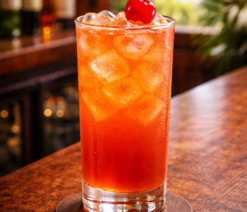A sex with the captain cocktail recipe served in a highball glass with ice and cherry garnish on a bar counter.