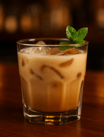 Nutty Bitch cocktail recipe in an old-fashioned glass with ice and mint garnish on a light wooden bar