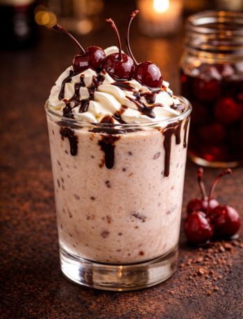 A my busted cherry cocktail recipe served in an old fashioned glass topped with whipped cream, chocolate drizzle, and rum soaked cherries.